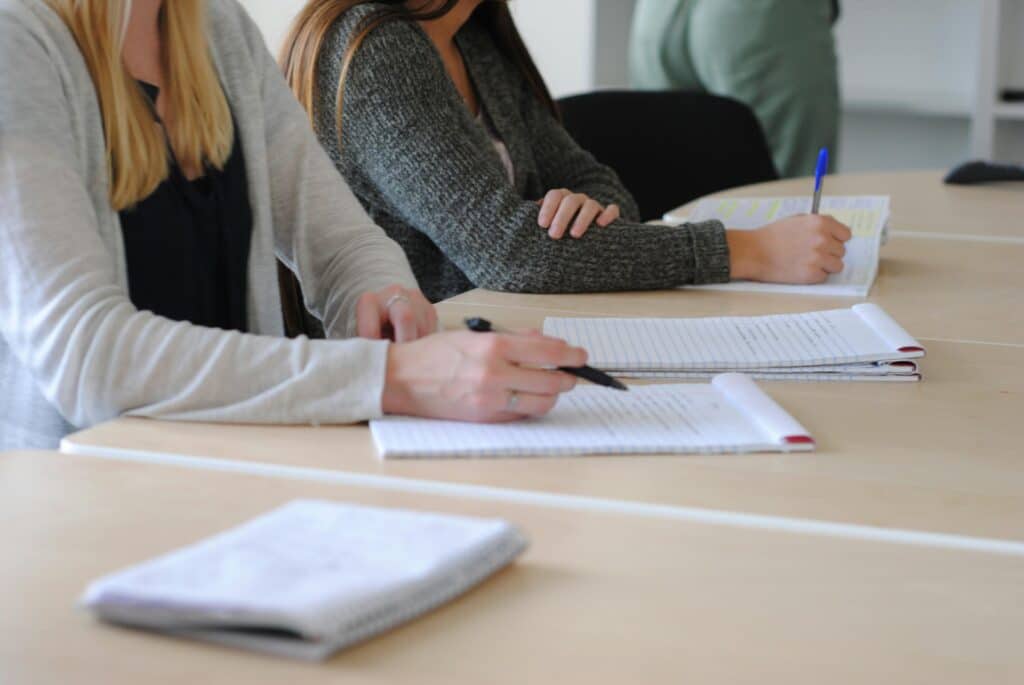 Group of students writing notes at a meeting in a well-lit classroom.